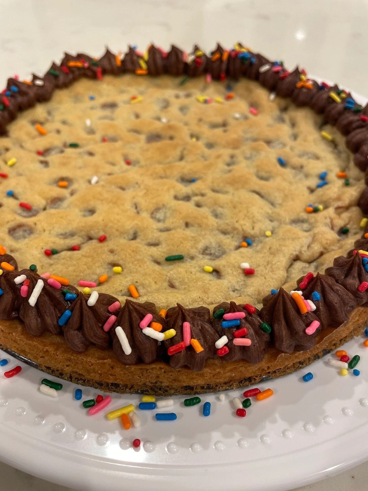 Cookie cake with a chocolate frosting border and rainbow sprinkles