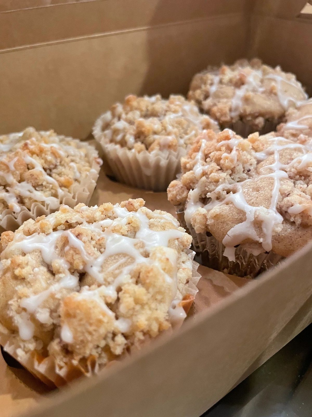 Crumb-topped muffins drizzled with icing in a bakery box