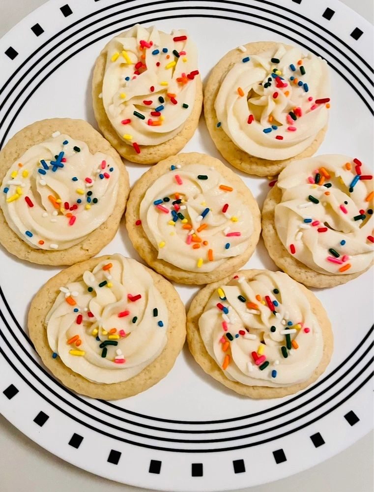 Vanilla-frosted sugar cookies with rainbow sprinkles on a striped plate