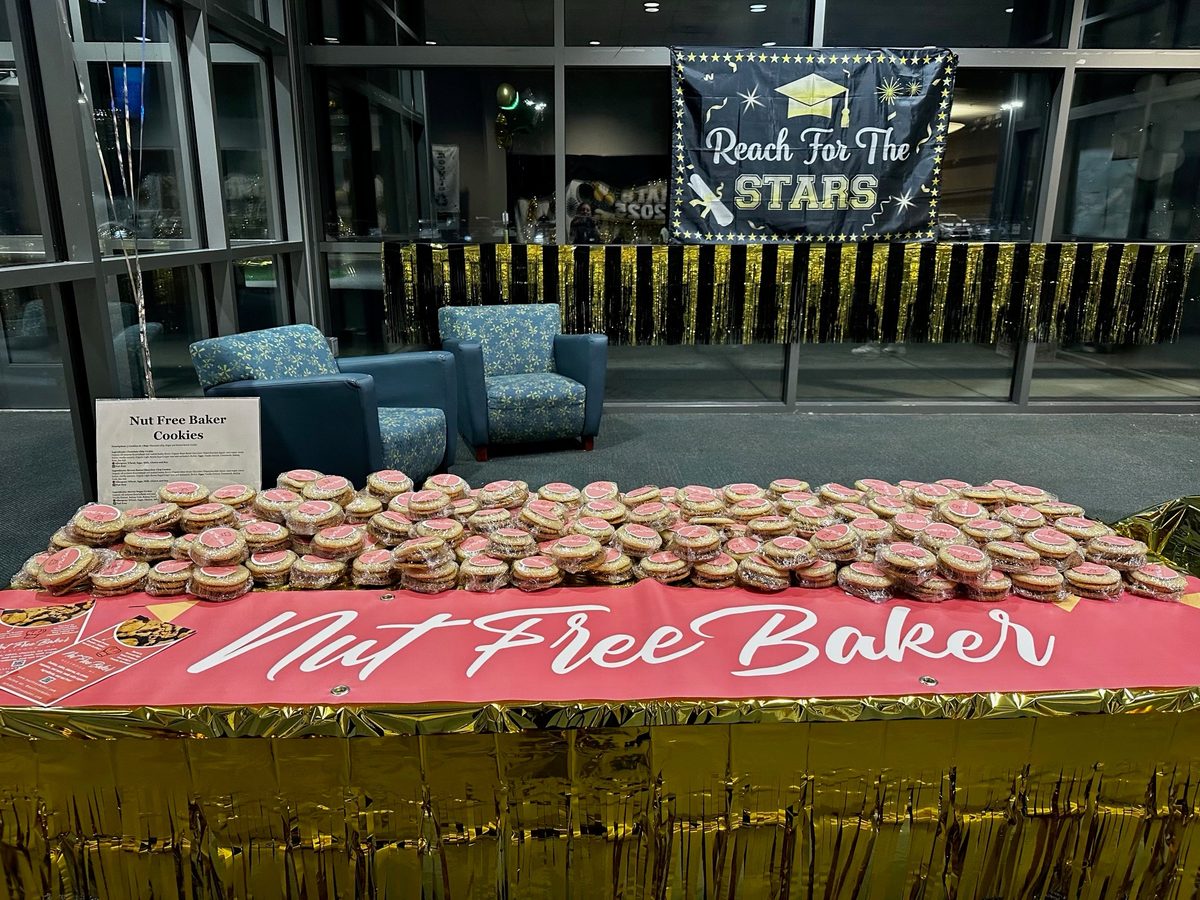 A long table of individually wrapped cookies with pink Nut Free Baker labels at a graduation party